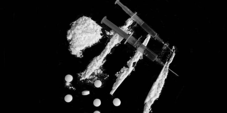 Injection syringe on cocaine drug powder lines, pile and pills on black background (//iStock)