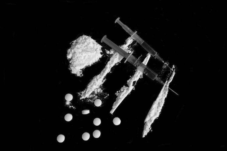 Injection syringe on cocaine drug powder lines, pile and pills on black background (//iStock)