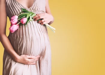 Beautiful pregnant woman with tulips flowers holds hands on bell