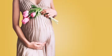 Beautiful pregnant woman with tulips flowers holds hands on bell