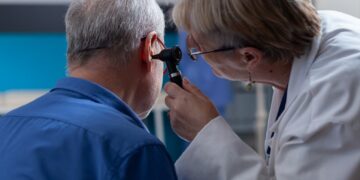 Médica examinando o ouvido de um paciente com otoscópio