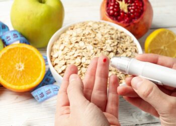 Pessoa medindo glicose no dedo com alimentos saudáveis ao redor.