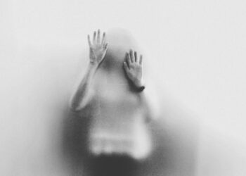 Pessoa com as mãos apoiadas em vidro fosco, vista em silhueta desfocada