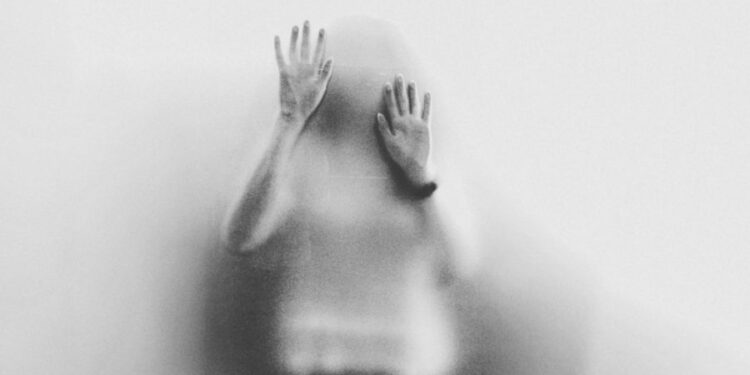 Pessoa com as mãos apoiadas em vidro fosco, vista em silhueta desfocada
