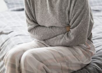 Pessoa sentada na cama segurando o abdômen em sinal de dor