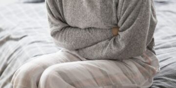 Pessoa sentada na cama segurando o abdômen em sinal de dor