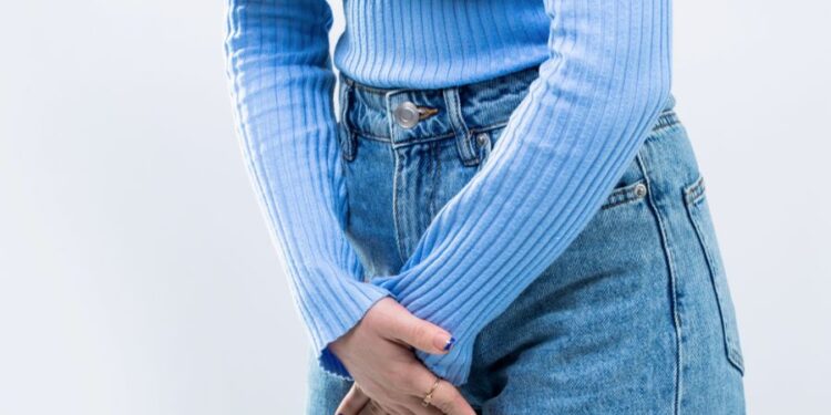 Mulher com as mãos sobre a região pélvica em sinal de desconforto.