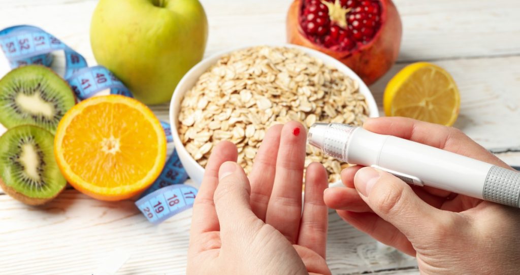 Pessoa medindo glicose no dedo com alimentos saudáveis ao redor.