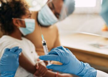 Criança usando máscara sendo preparada para vacinação por profissional de saúde