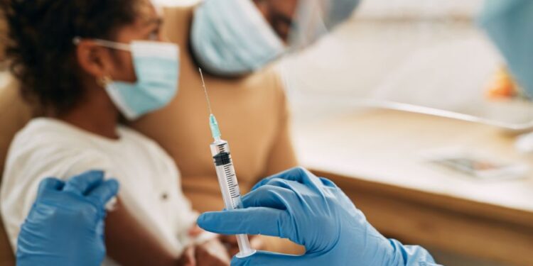 Criança usando máscara sendo preparada para vacinação por profissional de saúde