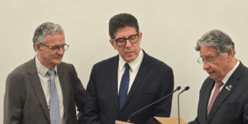 Foto de três homens. À direita, um deles fala ao microfone e toma posse como membro titular da Academia de Medicina de São Paulo.