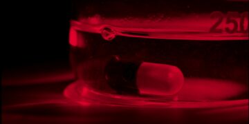 Foto em tons de vermelho da borda de um copo. Dentro, um comprimido submerso.