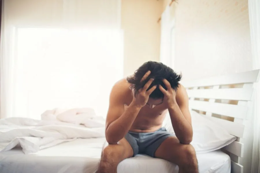Homem sentado na cama com expressão de preocupação.