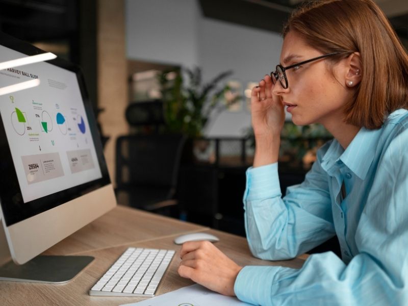 Pessoa de óculos analisando gráficos em um computador no escritório.