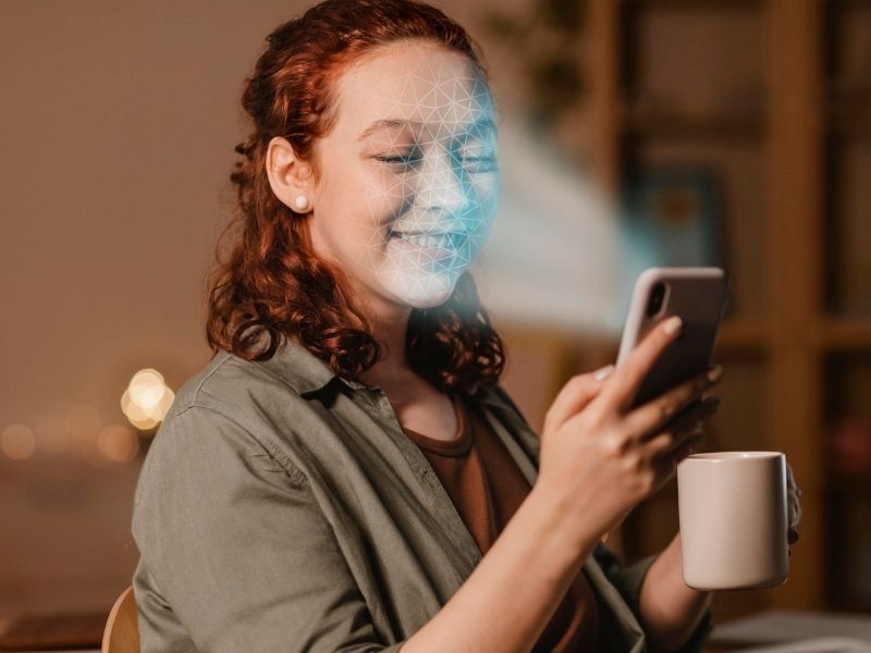 Pessoa sorrindo enquanto usa o celular, com efeito de reconhecimento facial no rosto.