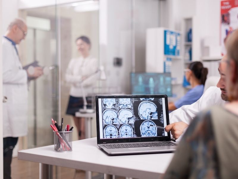 Profissionais de saúde analisando exames de imagem do cérebro em um laptop.