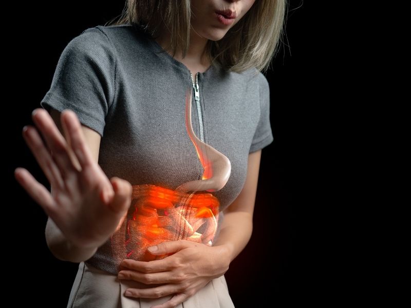 Pessoa segurando o abdômen com ilustração do estômago em destaque, indicando desconforto.