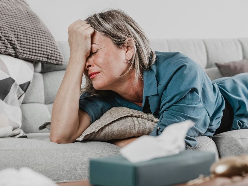Pessoa deitada no sofá com a mão na cabeça, aparentando cansaço ou tristeza.