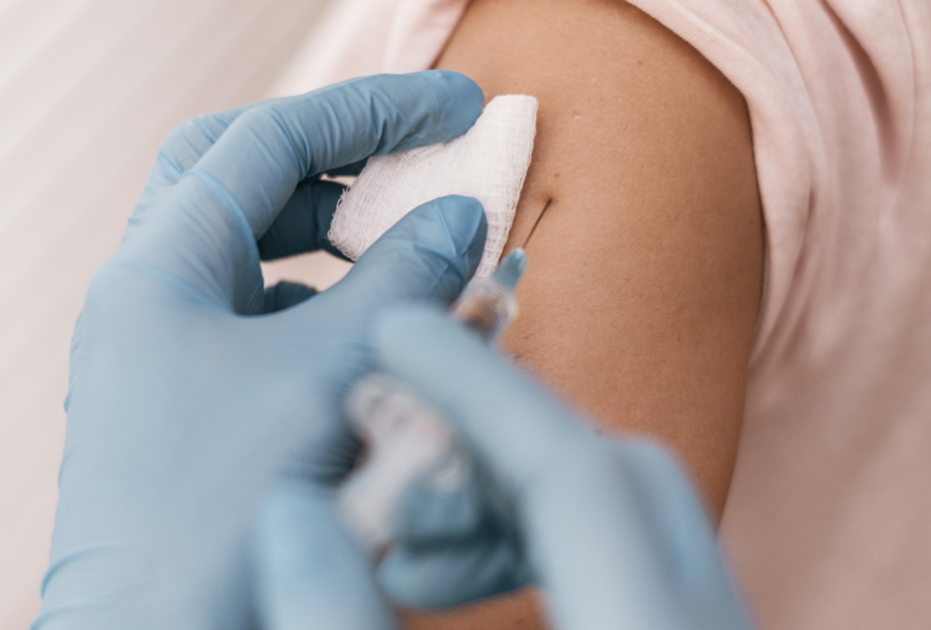 Aplicação de vacina no braço com seringa e luvas descartáveis.