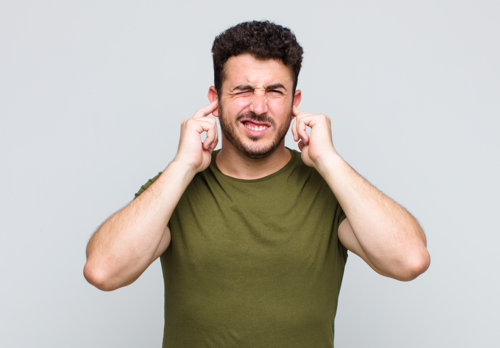 Homem tampando os ouvidos com expressão de incômodo por barulho