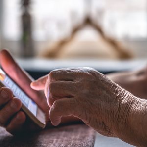 Hands of an elderly woman holding a mobile phone, close up.